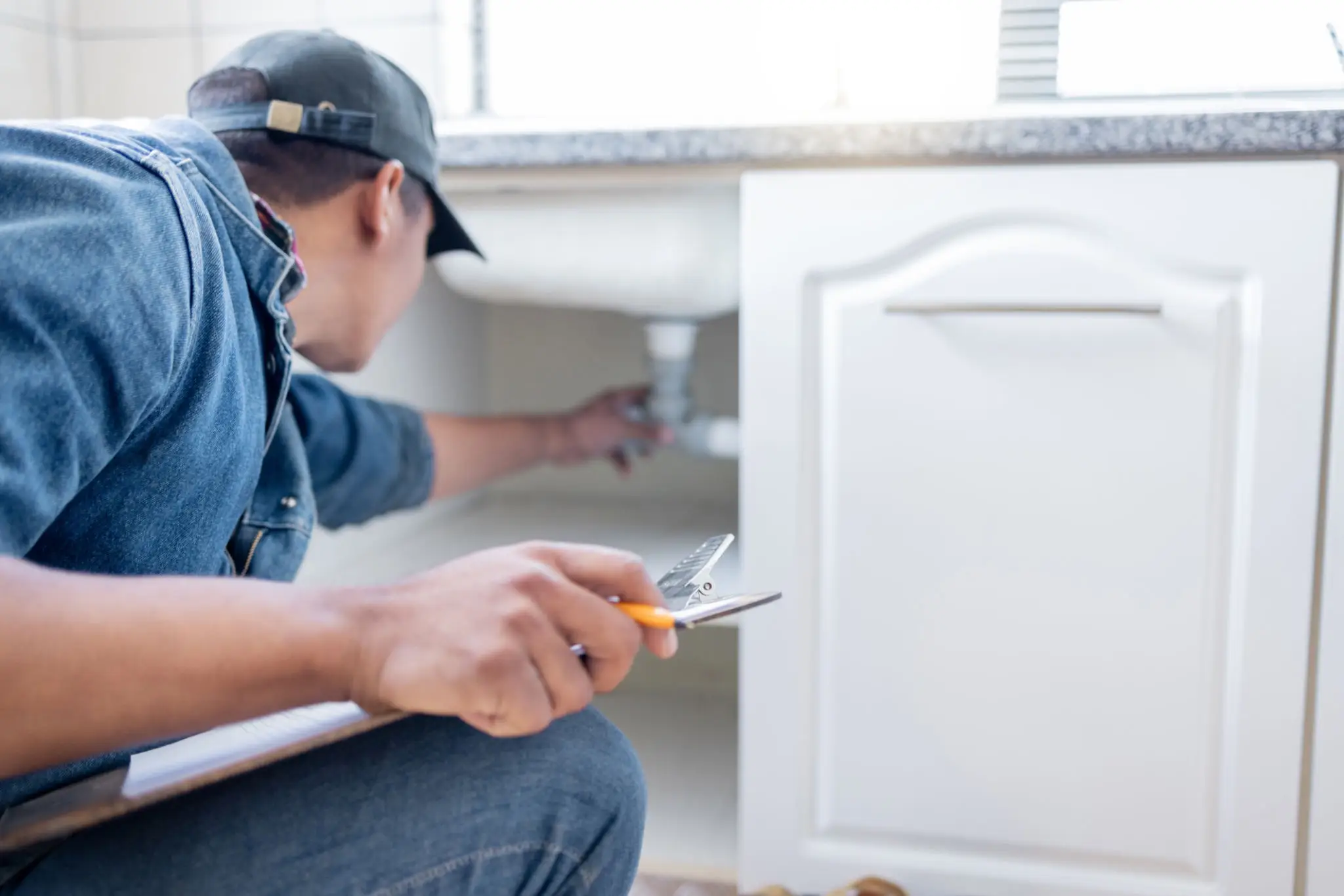 Plumber repairing sink under kitchen counter.