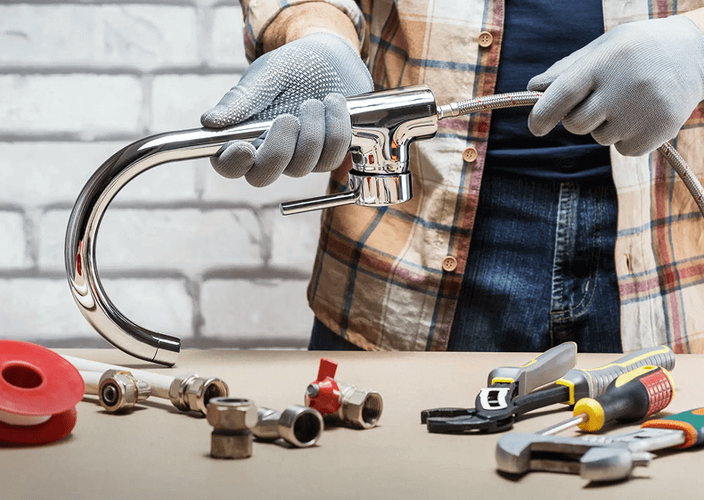Person holding faucet, surrounded by plumbing tools.